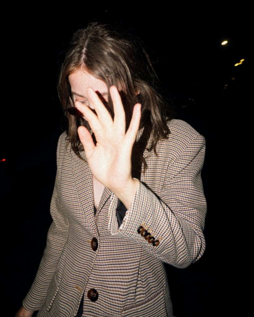woman covering her face in a houndstooth patterned blazer